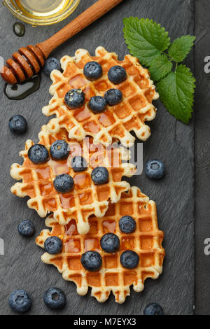 Belgische Waffeln mit Honig und frischen Beeren Heidelbeeren und Minze auf schwarzen Oberfläche. Köstliches Dessert Stockfoto