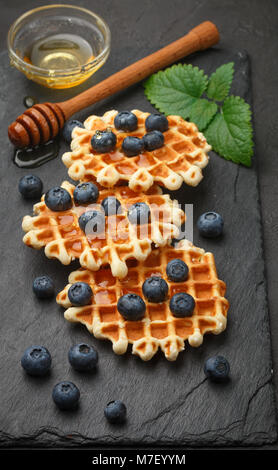 Wiener Waffeln mit Honig und frischen Beeren Heidelbeeren und Minze auf schwarzen Oberfläche. Köstliches Dessert Stockfoto