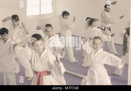 Gruppe junger Kinder Karate Tritte mit männlichen Trainer während Karate Klasse Stockfoto