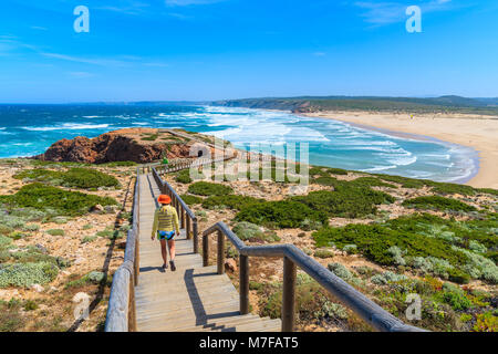 Junge Frau touristische Aufwachen auf hölzernen Gehweg zu schönen Praia da bordeira Strand, beliebter Ort Kitesurfen zu tun, Algarve, Portuga Stockfoto