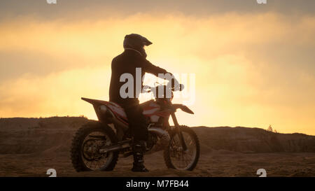 Professionelle FMX Motorradfahrer ruht auf seinem Fahrrad und blickt auf harte Sandy Off-Road Gelände. Sun Einstellung ist. Stockfoto