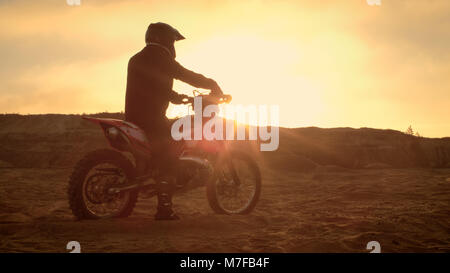 Professionelle FMX Motorradfahrer ruht auf seinem Fahrrad und blickt auf harte Sandy Off-Road Gelände. Sun Einstellung ist. Stockfoto