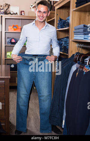 Junger Mann ist die Auswahl an neuen Jeans in der Kleidung der Männer zu speichern. Stockfoto