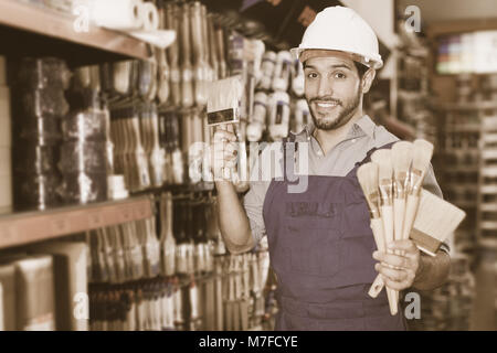 Happy Vorarbeiter in blauen Overalls Auswahl Pinsel in Farbe Speicher Stockfoto