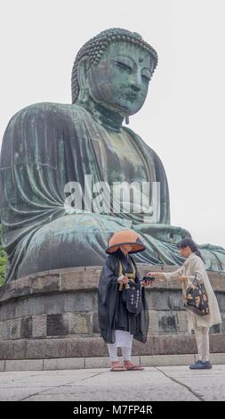 Japanische Frau Geld in Schwarz lackierte Schale mit japanischer buddhistischer Pilger vor Kamakura Buddha läutenden Glocke und singen Sutras. Stockfoto