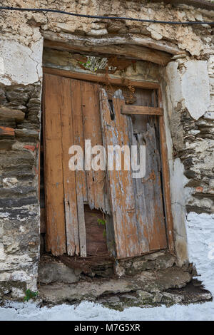 Eine alte Holztür mit vielen Schäden sichtbar auf der Vorderseite eines verlassenen Hauses im Dorf Sayalonga in Andalusien, Spanien. Stockfoto