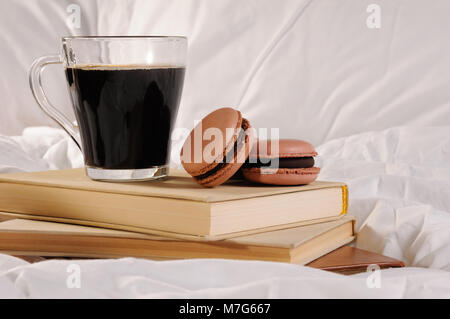 Morgendlichen Tasse Kaffee mit Schokolade Kuchen Makronen, auf einem Stapel Bücher im Bett. Stockfoto