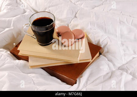 Morgendlichen Tasse Kaffee mit Schokolade Kuchen Makronen, auf einem Stapel Bücher im Bett. Stockfoto