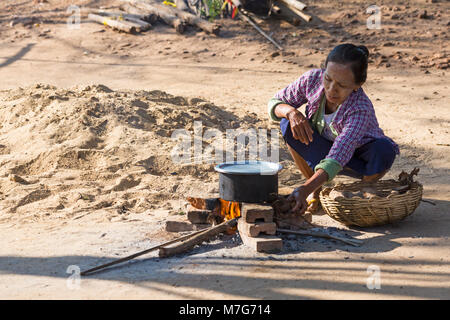 Lokale Frau mit Pan auf offenem Feuer kochen außerhalb in Bagan, Myanmar (Birma), Asien im Februar Stockfoto