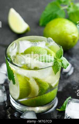 Kalt Erfrischende Sommer trinken mit Limette, Minze und Eiswürfel in einem Glas auf einem dunklen Stein Hintergrund. Mojito. Limonade. Detox. Mineralwasser. Selektive fo Stockfoto