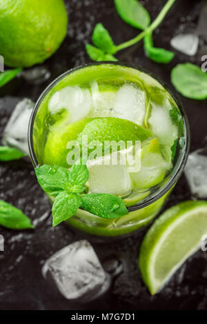 Kalt Erfrischende Sommer trinken mit Limette, Minze und Eiswürfel in einem Glas auf einem dunklen Stein Hintergrund. Mojito. Limonade. Detox. Mineralwasser. Selektive fo Stockfoto