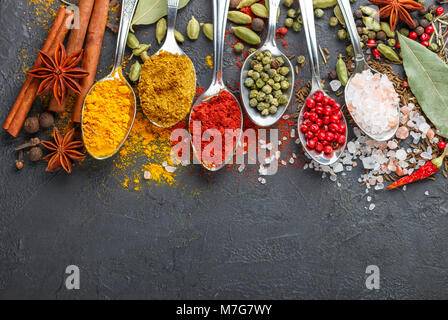 Vielfalt der natürlichen Gewürze, Gewürze und Kräuter in der Löffel auf den steinernen Tisch - Paprika, Curry, Koriander, Kardamom, Kurkuma, Rosmarin, Salz, Pfeffer, Stockfoto