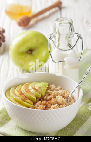 Bio Haferflocken in eine keramische Schüssel mit Apfel, Zimt und Honig auf weissem Holztisch. Gesundes Frühstück - das Konzept der richtigen Ernährung und Diät Stockfoto