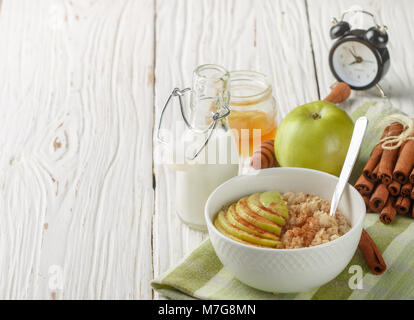 Bio Haferflocken in eine keramische Schüssel mit Apfel, Zimt und Honig auf weissem Holztisch. Gesundes Frühstück - das Konzept der richtigen Ernährung und Diät Stockfoto
