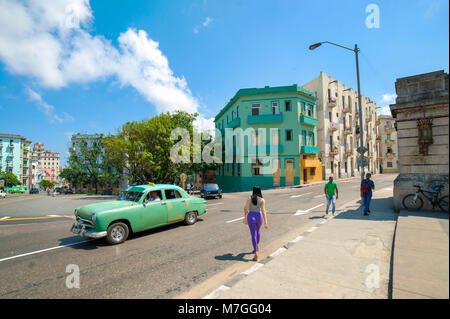 Eine junge Frau kreuzt eine Straße neben einem klassischen Taxi in Havanna, Kuba Stockfoto