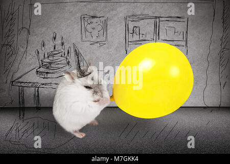 Hamster bläst auf einen gelben Ballon, auf dem Hintergrund seiner bemalte Zimmer neben einem Tisch, auf dem ein Kuchen, ein Konzept von einem Urlaub, Geburtstag Stockfoto