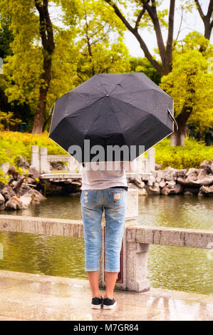 Eine Frau mit einem Regenschirm innerhalb von Li Yuan, einem traditionellen, chinesischen Garten, in Zhaojialou Stadt in Shanghai, China. Stockfoto