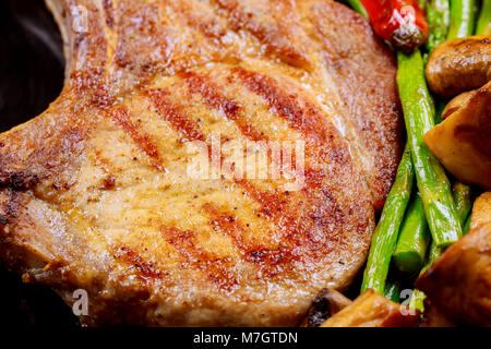 Gegrilltes Steak vom Schwein mit Spargel und Champignons mit Kräutern, Braten auf Stein Schiefer Hintergrund schliessen. Warme Gerichte Stockfoto