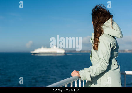 Junge reisende Frau suchen das Meer, Segeln eine Fähre, mit Big Boat Cruise Liner oder Fähre auf dem Hintergrund, trägt eine Regenjacke. Stockfoto