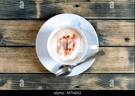 Blick von oben auf eine Tasse Kaffee mit Milch mit Kakao auf einem antiken Holztisch. Stockfoto