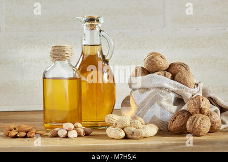 Konzeptionelle Zusammensetzung von Glas Öl Gläser mit verschiedenen Arten von Nüssen auf Holztisch, close-up. Studio gedreht. Aromatische und gesunde Dressing. Nutriti Stockfoto