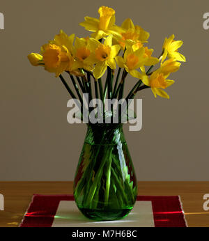 Gelbe Narzissen in eine grüne Vase auf einem Tisch in der Nähe eines Fensters. Stockfoto