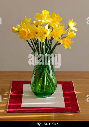 Gelbe Narzissen in eine grüne Vase auf einem Tisch in der Nähe eines Fensters. Stockfoto