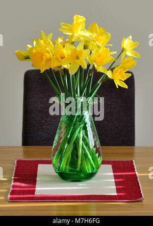 Gelbe Narzissen in eine grüne Vase auf einem Tisch in der Nähe eines Fensters. Stockfoto