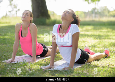 Zwei junge Frauen, die Fit Pilates Übung Anheben der oberen Partie des Seitenteils im Freien Stockfoto