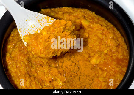 Pilav auf einem weißen Löffel, auf dem Hintergrund der multicooker mit einem Teller Stockfoto