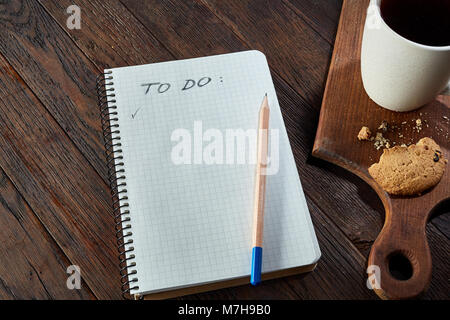 Tasse Tee mit Chocolate Chips cookies, Arbeitsmappe mit in es und einen gelben Bleistift auf einem hölzernen Schneidebrett über vintage Hintergrund tun, oben vie Stockfoto