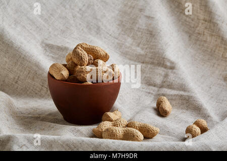 Ungeschälte Erdnüsse in Ton Keramik Schüssel closeup, selektive konzentrieren. Gesunde und nahrhafte Zwischenmahlzeit. Köstliche Zutat für Ihr jeden Tag kochen. Gesundheit Stockfoto