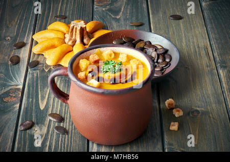 Leckere Kürbissuppe in alten Emaille Tasse auf rustikalen Holztisch. Die Suppe mit Croutons, Petersilie und Kürbiskernöl serviert. Stockfoto