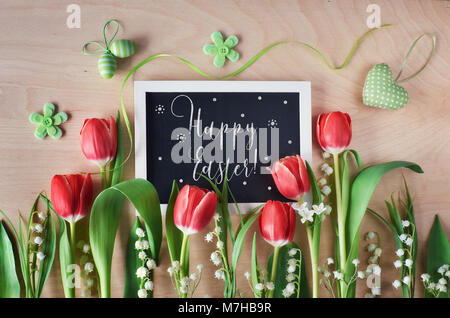 Ostern Zusammensetzung mit Blackboard mit Frühling Blumen, Tulpen und Maiglöckchen eingerahmt. Text "Frohe Ostern" an die Tafel. Stockfoto