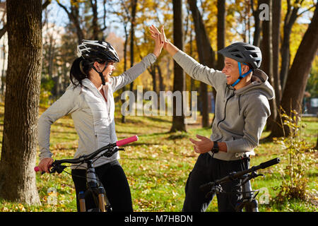 Glücklich lächelnde junge Paar tragen healmets und Sportswear für eine Radtour auf einem sonnigen warmen Herbst Tag im Park. Sie sind gemeinsam Spaß zu haben. Stockfoto