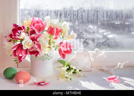 Rosa Tulpen und weiße Freesie Blumen mit Ostern Dekorationen auf dem Fenster, Sonne nach dem Regen Stockfoto