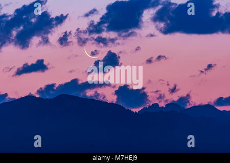 Abnehmende Mondsichel in der Morgendämmerung über dem Grand Tetons in Wyoming. Stockfoto