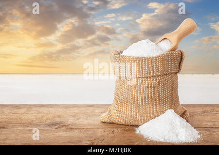Salz in der Tasche. Kristalle von Salz in Sack auf Tabelle mit salzigen See im Hintergrund. Beutel mit Meersalz auf der Farm hergestellt Stockfoto