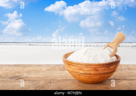 Salz in der Schüssel. Kristalle von Salz in Ton Schüssel auf Tabelle mit salzigen See im Hintergrund. Meersalz produziert auf der Farm Stockfoto