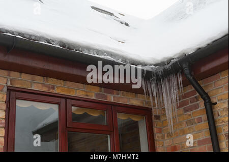 Leichte Erwärmung von Haus Dach und schmelzende Schnee und Eiszapfen Anhäufung in gefrorenen Dachrinnen und mögliche Eindringen von Wasser in die Wände Stockfoto