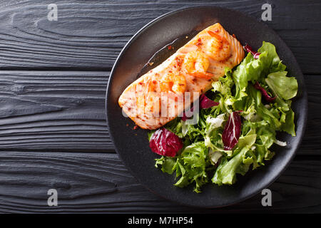 Gebackenen Lachs mit Krabben und Honig Sauce mit Beilage Salat mix Close-up auf einem Teller auf dem Tisch. Horizontal oben Ansicht von oben Stockfoto