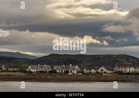 Nach Aultbea, Schottland - Juni 8, 2012: ruhiges Wasser von Loch Ewe mit der Gemeinschaft der Aultbea unter dunklen regnerischen cloudscape. Dunkle Hügel im Hintergrund. Stockfoto