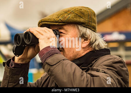 Hereford, Herefordshire, UK. 10. März, 2018. Ein Mann wacht ein Rennen durch ein Fernglas bei Hereford Pferderennbahn während der Ladies Tag in Hereford am 10. März 2018. Quelle: Jim Holz/Alamy leben Nachrichten Stockfoto