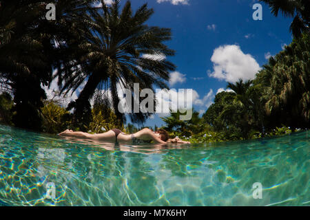 Eine Frau liegt am Rande eines Infinity-Pool mit einem tropischen Hintergrund auf der Insel Curacao, Niederländische Antillen, in der Karibik. Stockfoto