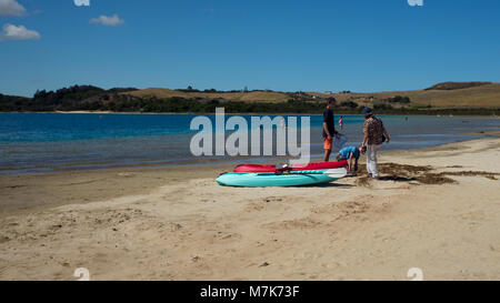 Zwei Jungen graben ein Loch in den Sand neben ihrem Kajak am Ufer See Kia Iwi sprechen mit einer Frau. Stockfoto