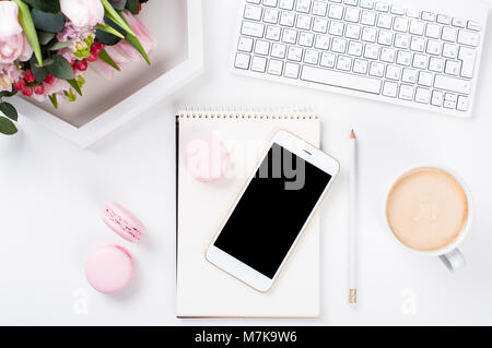 Lady blogger Schreibtisch mit rosa Blüten und Macaron Kuchen auf weißem Hintergrund, weiblich Home Office workspce mit Kaffee und Smartphone Mock-u Stockfoto
