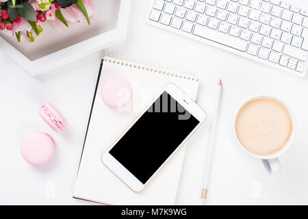 Lady blogger Schreibtisch mit rosa Blüten und Macaron Kuchen auf weißem Hintergrund, weiblich Home Office workspce mit Kaffee und Smartphone Mock-u Stockfoto