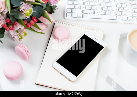 Lady blogger Schreibtisch mit rosa Blüten und Macaron Kuchen auf weißem Hintergrund, weiblich Home Office workspce mit Kaffee und Smartphone Mock-u Stockfoto
