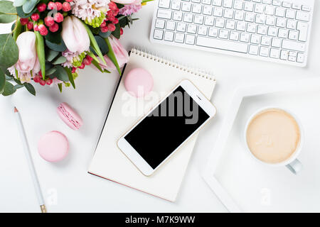 Lady blogger Schreibtisch mit rosa Blüten und Macaron Kuchen auf weißem Hintergrund, weiblich Home Office workspce mit Kaffee und Smartphone Mock-u Stockfoto