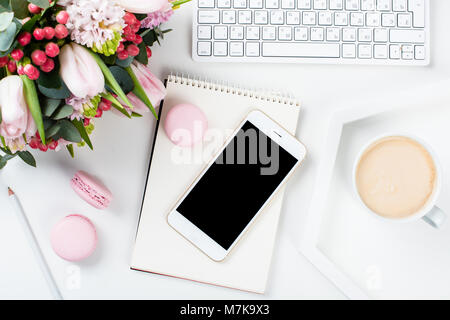Lady blogger Schreibtisch mit rosa Blüten und Macaron Kuchen auf weißem Hintergrund, weiblich Home Office workspce mit Kaffee und Smartphone Mock-u Stockfoto